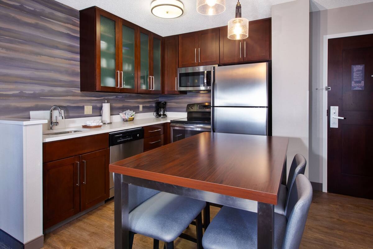 A modern kitchen with wooden cabinets, stainless steel appliances, and a dining table with chairs.