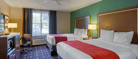 A hotel room with two beds, a desk with a chair, a ceiling fan, and a large window with curtains.