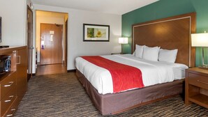 A hotel room with a large bed, a wooden headboard, a desk with a lamp, a television, and a framed picture on the wall. - Comfort Inn West Valley Salt Lake City South (West Valley City)