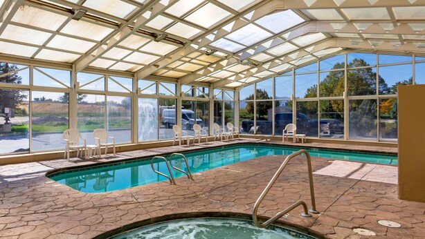 An indoor swimming pool with clear glass walls, a hot tub, and lounge chairs. - Comfort Inn West Valley Salt Lake City South (West Valley City)