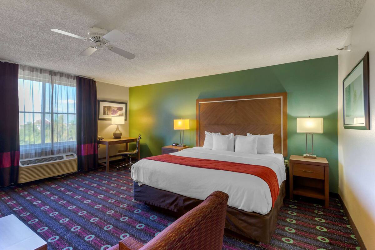 Ein Hotelzimmer mit Bett, Nachttischen, Schreibtisch, Stuhl, Deckenventilator und einem Fenster mit Vorhängen.