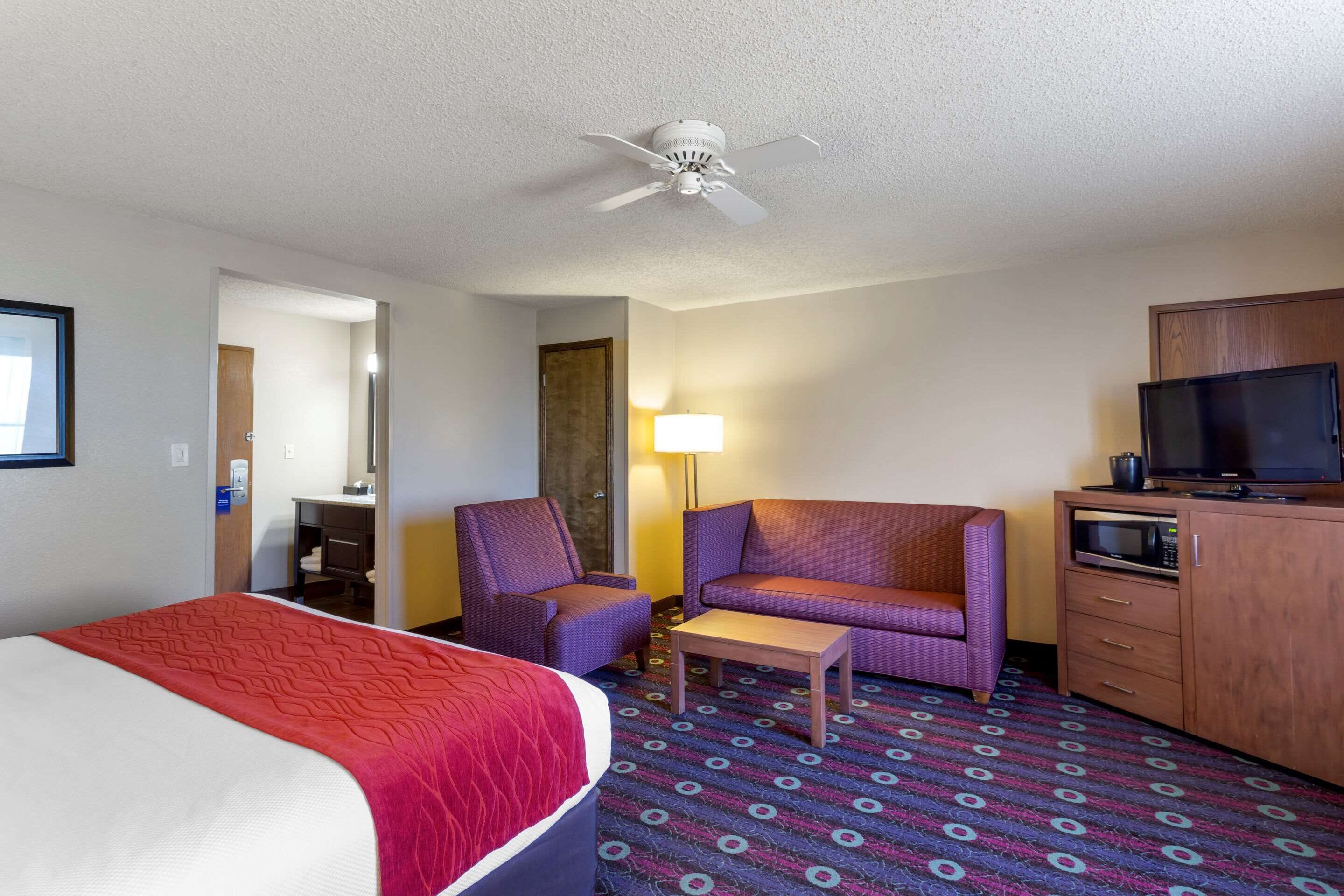 A hotel room with a bed, two armchairs, a small table, a TV, and a microwave.