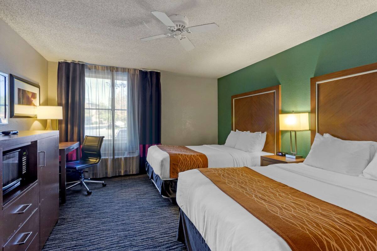 Ein Hotelzimmer mit zwei Betten, einem Schreibtisch mit Computer, einem Stuhl und einer Mikrowelle.