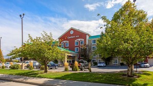 A Comfort Inn hotel with a red facade, multiple windows, and a green awning. There are trees in front of the building and parked cars in the parking lot. - Comfort Inn West Valley Salt Lake City South (West Valley City)