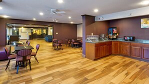 A hotel lobby with a wooden floor, a seating area with chairs and tables, a kitchenette, and a ceiling fan. - Comfort Inn West Valley Salt Lake City South (West Valley City)