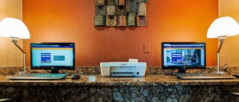A hotel reception desk with two computer monitors, a Canon printer, and two lamps.