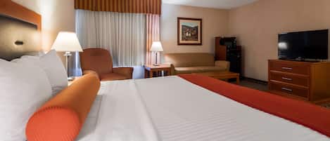 A hotel room with a large bed, two armchairs, a sofa, a TV, a desk, and a painting on the wall.