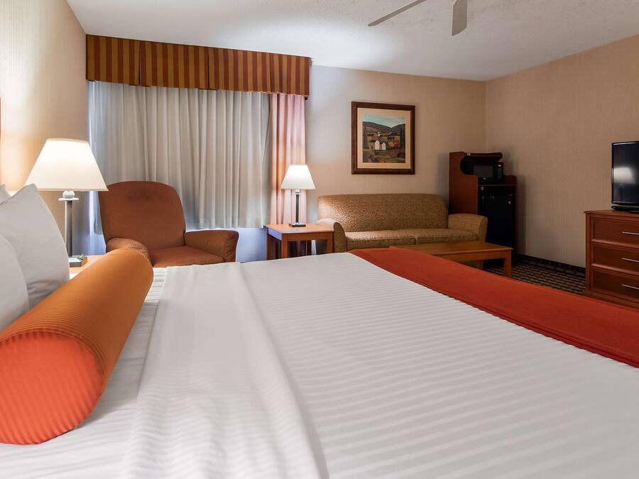 Una habitación de hotel con una cama grande, dos sillones, un sofá, un televisor, un escritorio y un cuadro en la pared.