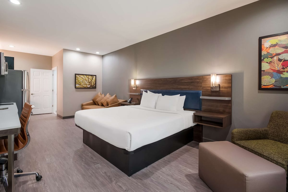 A modern hotel room with a large bed, a desk, a chair, and a couch.