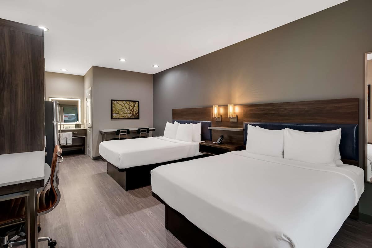 A hotel room with two beds, a desk, a chair, a mirror, and a wall-mounted TV.