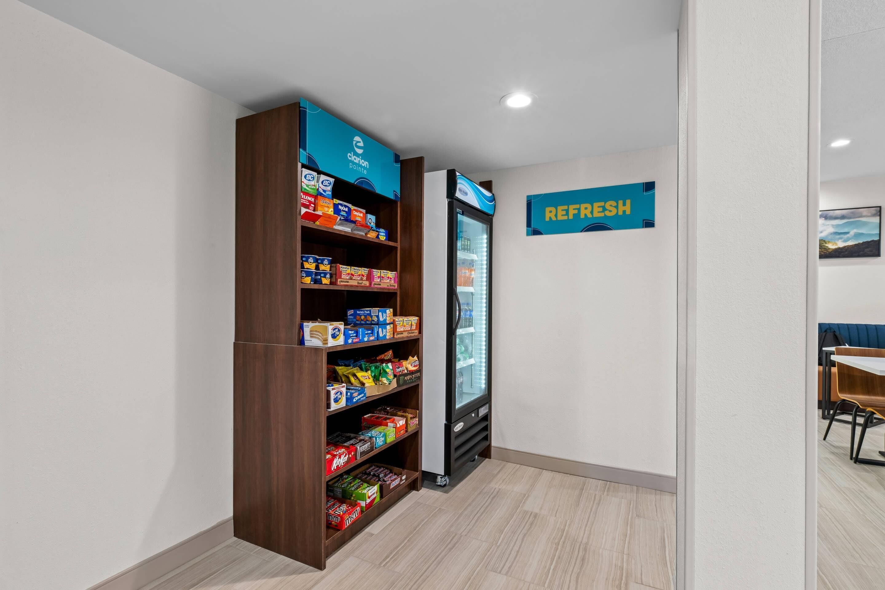 Máquina expendedora llena de aperitivos y una vitrina refrigerada en una habitación moderna y luminosa, con suelo de madera clara y paredes blancas.