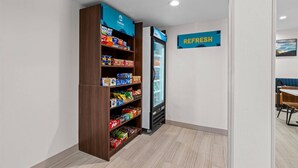 A vending machine stocked with snacks and a refrigerated display unit in a clean, modern room with light wood flooring and white walls.