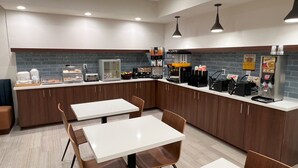 A modern kitchen with white countertops, wooden cabinets, and a seating area with tables and chairs. - Clarion Pointe (High Point)
