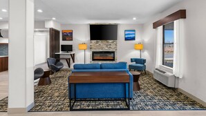 A modern living room with a blue sofa, a wooden coffee table, and a fireplace. There are two lamps, a TV, and a window with curtains. - Clarion Pointe (High Point)