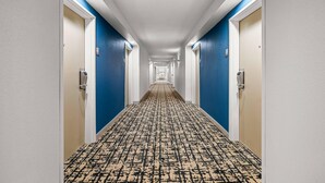 A hotel hallway with blue walls, white doors, and a patterned carpet. - Clarion Pointe (High Point)