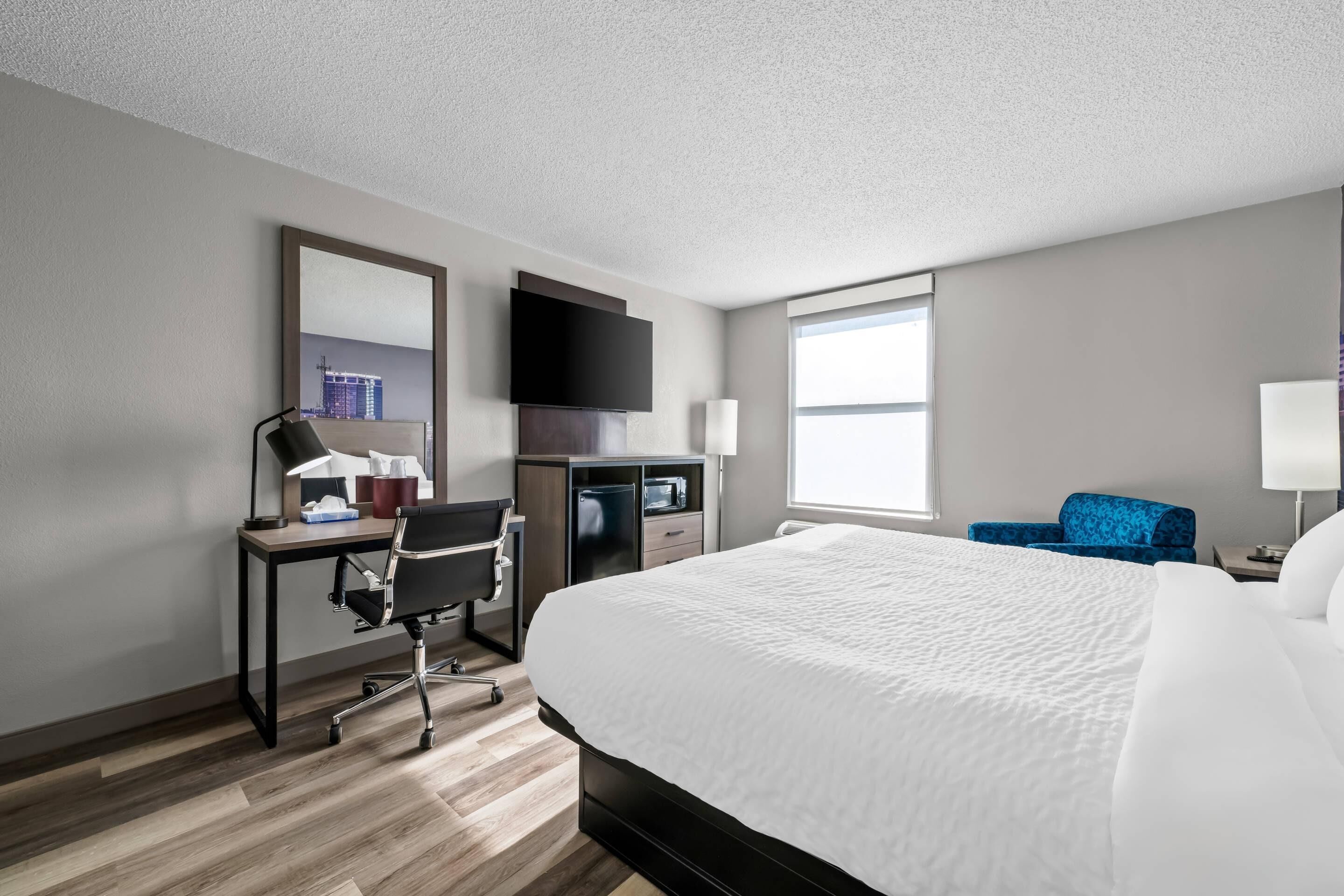 A hotel room with a bed, desk, chair, TV, and a window.