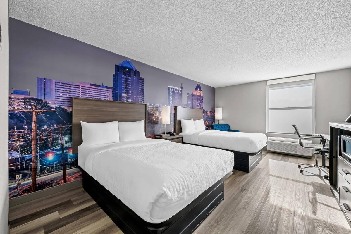 A hotel room with two beds, a desk, and a cityscape mural on the wall.