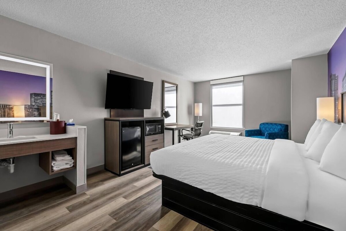 A hotel room with a bed, a desk, a television, and a cityscape view.