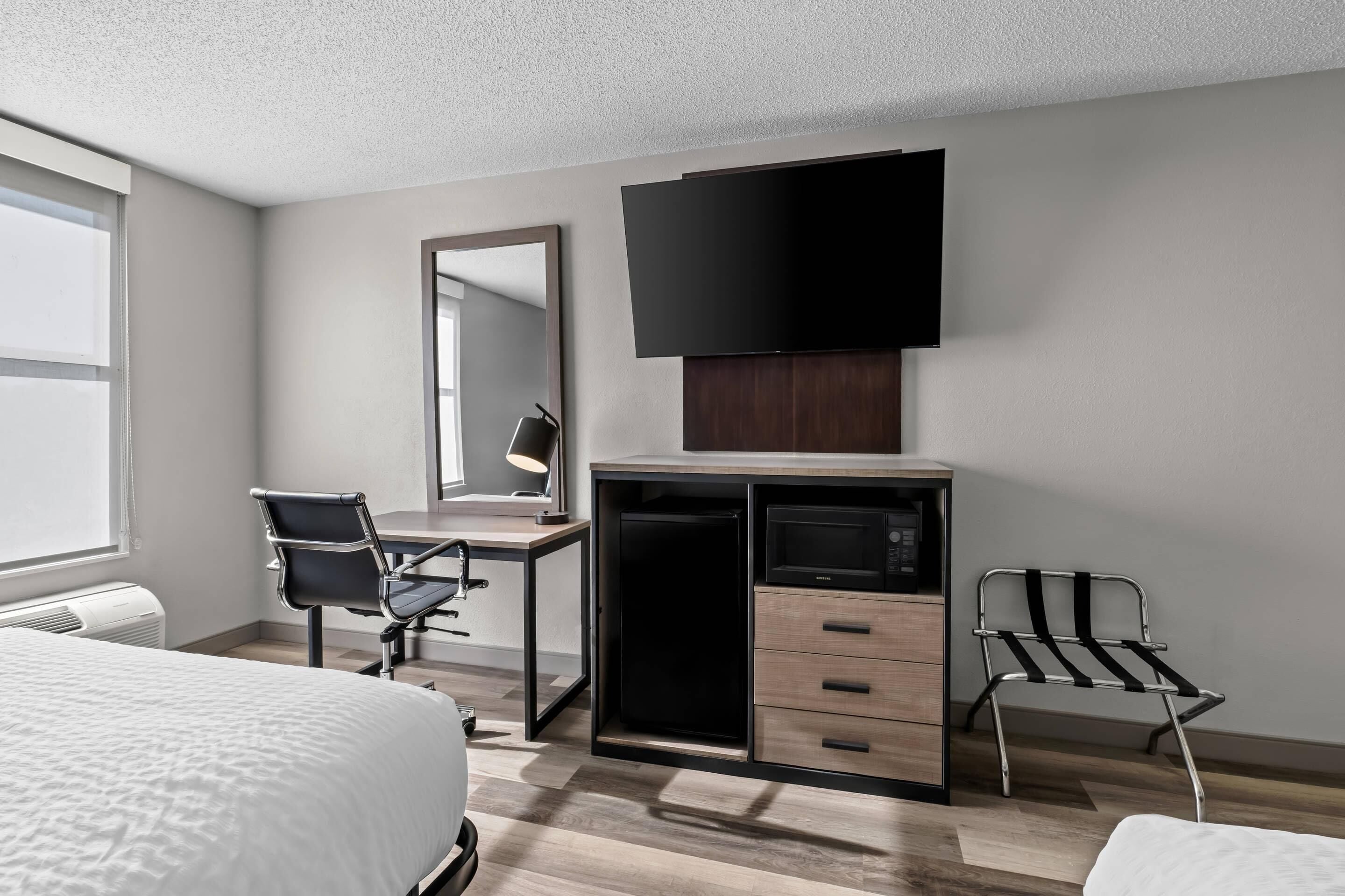 Een moderne hotelkamer met een bed, bureau, stoel, televisie en een ingebouwde magnetron.