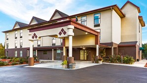 A multi-story hotel with a covered entrance, large windows, and a landscaped front yard. - Clarion Pointe (High Point)