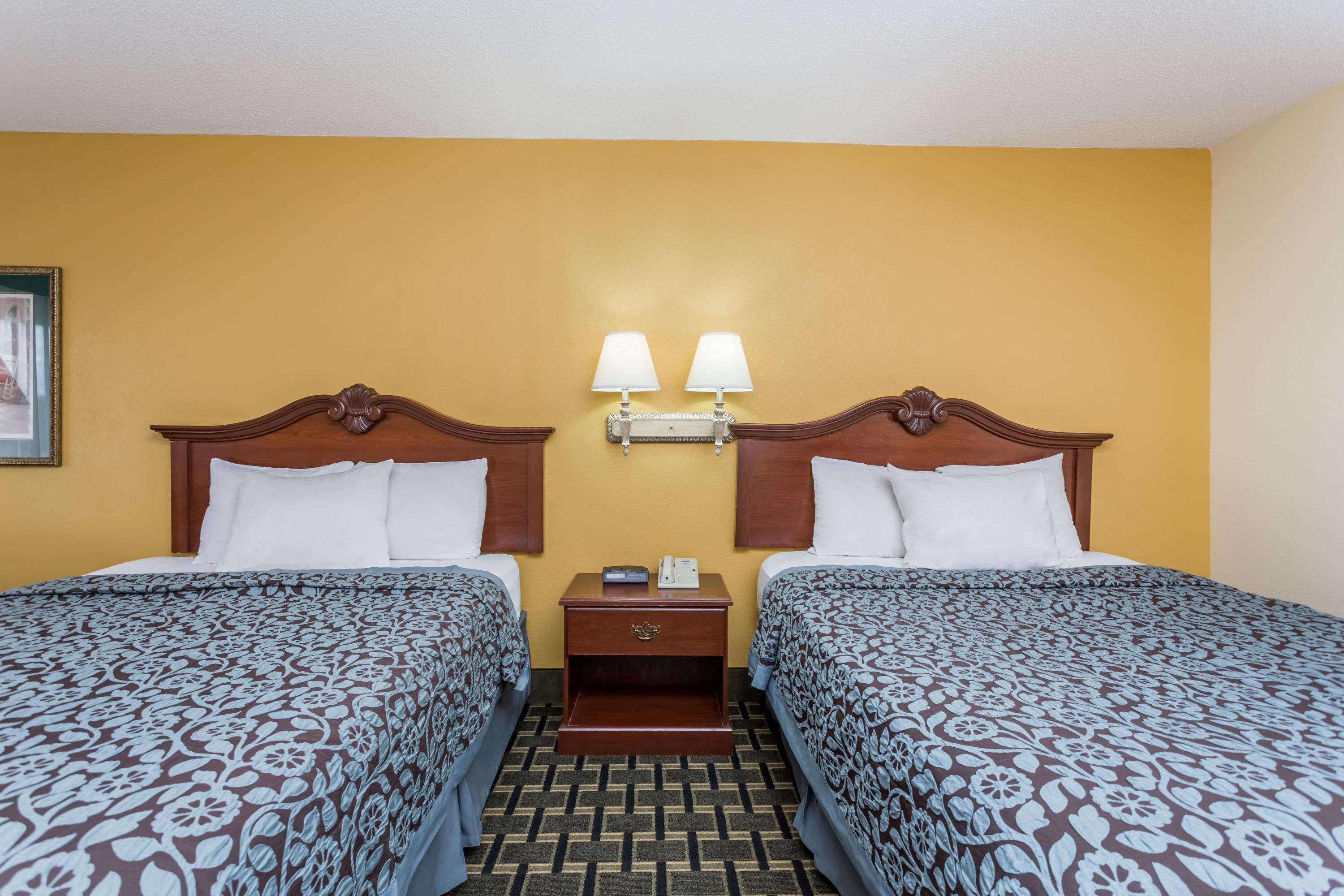 A hotel room with two beds, a nightstand with a lamp, and a wall-mounted light fixture.