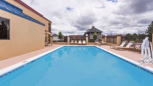 A swimming pool with lounge chairs and umbrellas, surrounded by buildings with a beige exterior and a red roof. - Days Inn & Suites by Wyndham Warner Robins Near Robins AFB (Warner Robins)