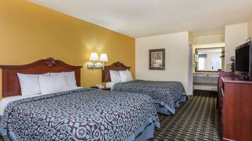 A hotel room with two beds, a wooden headboard, a nightstand, a TV, and a bathroom visible through an open door.