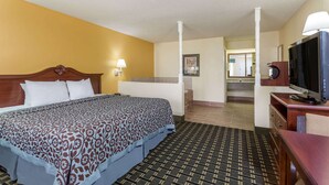 A hotel room with a large bed, a television, a desk, and a bathroom visible in the background. - Days Inn & Suites by Wyndham Warner Robins Near Robins AFB (Warner Robins)