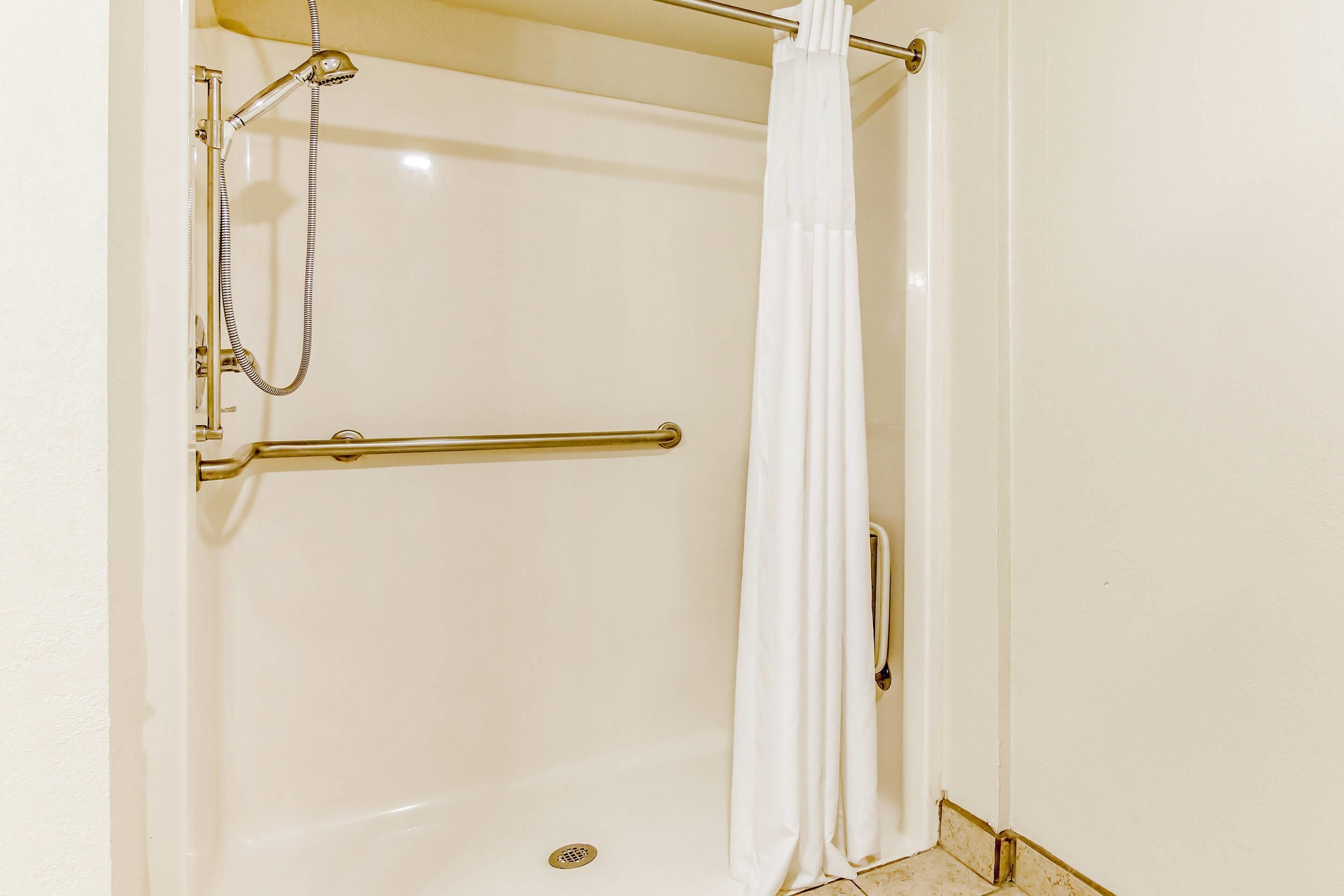 Un espace douche équipé d’une barre d’appui, d’un pommeau de douche et d’un rideau blanc.