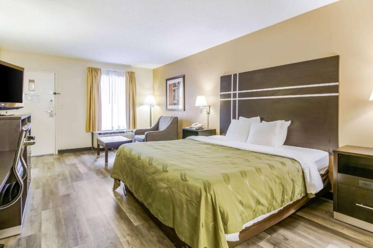 A hotel room with a bed, a desk, a chair, a television, and a bedside table.