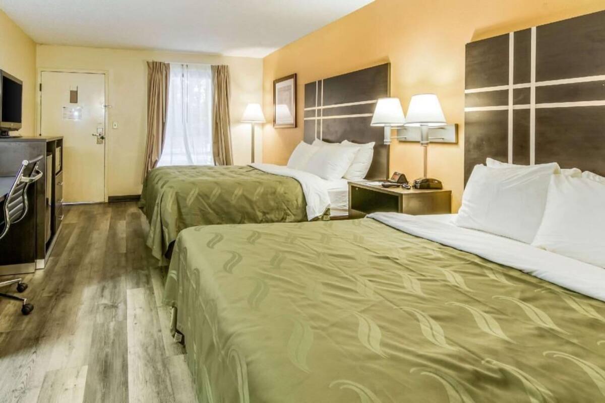 A hotel room with two beds, a desk, a TV, and a door.