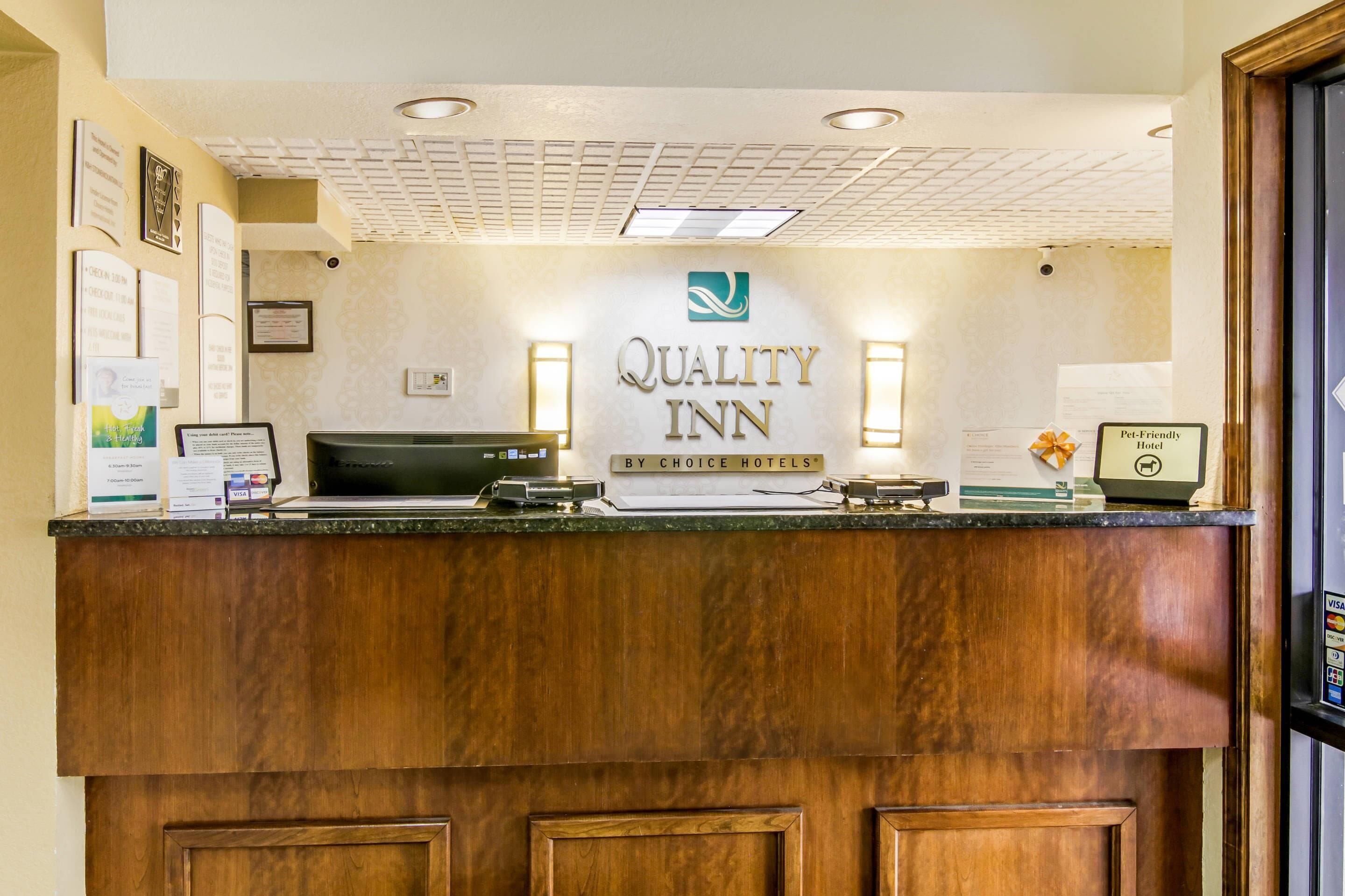 A hotel reception desk with a sign reading "Quality Inn" and "By Choice Hotels."