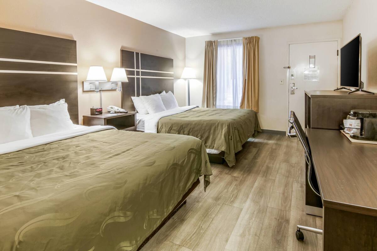Quarto de hotel com duas camas, uma escrivaninha, televisão e um minibar.