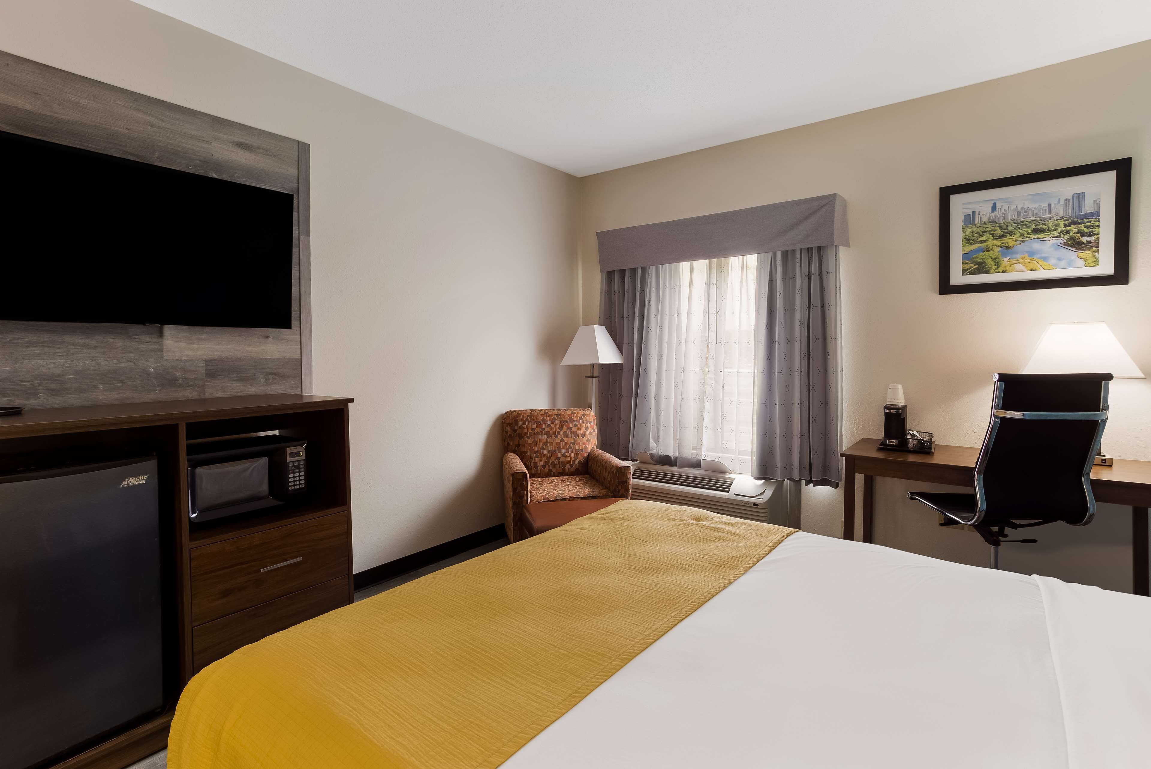 Une chambre d’hôtel équipée d’un lit, d’un bureau, d’une chaise, d’une télévision, d’un four à micro-ondes et d’une fenêtre avec des rideaux.