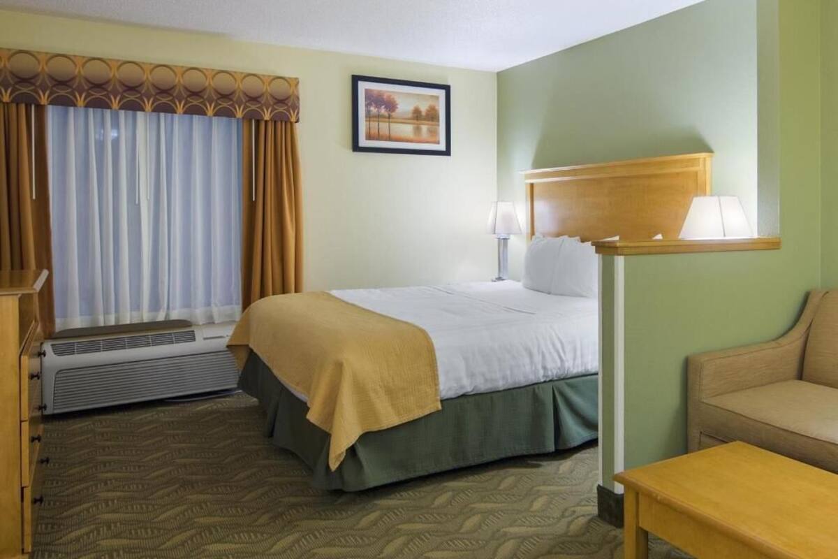 Une chambre d’hôtel avec un lit, un bureau, une chaise, une lampe et un tableau au mur.