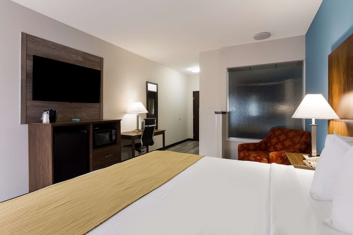 Une chambre d’hôtel avec un lit, un bureau et une chaise, une télévision, un four à micro-ondes et un fauteuil rouge.