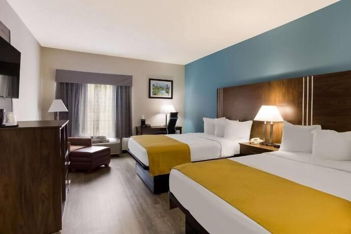 Une chambre d’hôtel avec deux lits, un bureau, une chaise, une télévision et une fenêtre avec des rideaux.