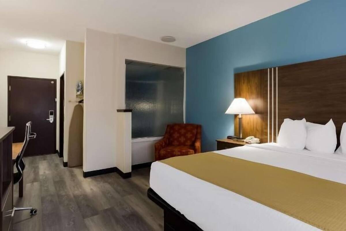 Une chambre d’hôtel comprenant un lit, un bureau, une chaise, une fenêtre et une table de chevet avec une lampe.