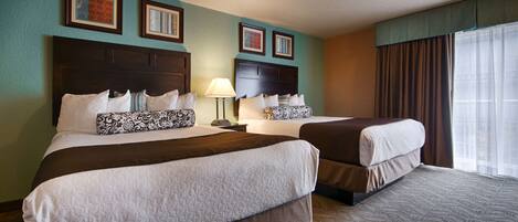 A hotel room with two beds, a nightstand, a lamp, and framed artwork on the walls.