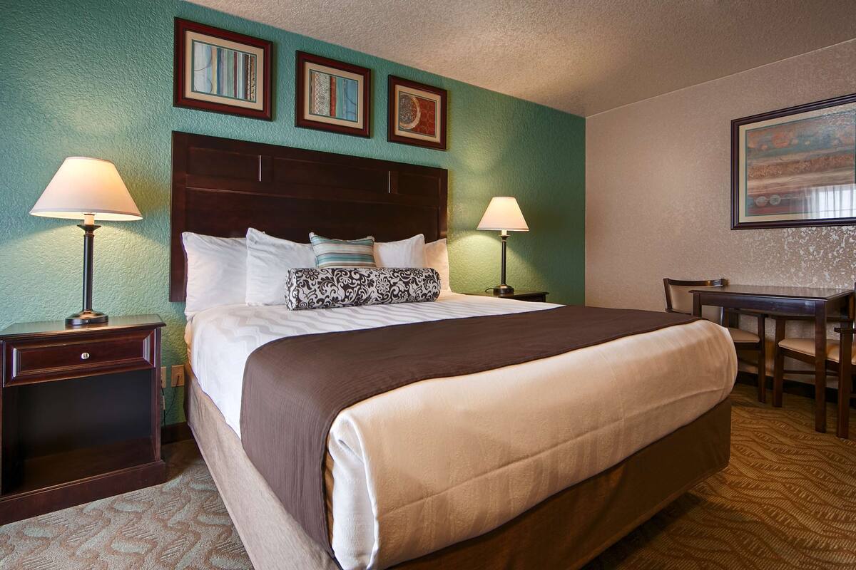 Quarto de hotel com uma cama grande, duas mesas de cabeceira, uma escrivaninha e uma cadeira.