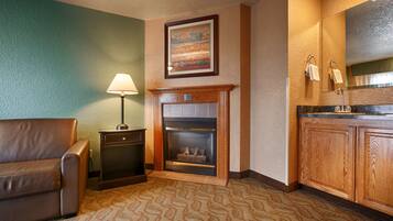 A hotel room with a fireplace, a lamp, a couch, and wooden cabinets.