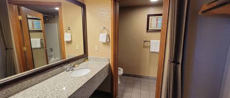 A bathroom with a granite countertop sink, a mirror, and a toilet.