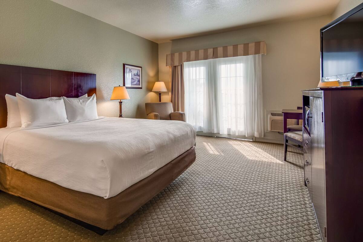 Quarto de hotel com uma cama grande, duas mesas de cabeceira com luminárias, um guarda-roupa e uma janela com cortinas.