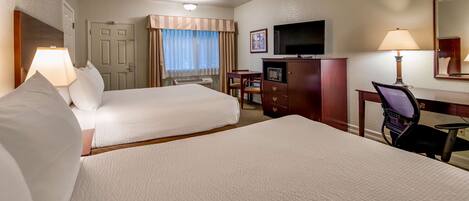 A hotel room with two beds, a desk, a TV, and a chair.