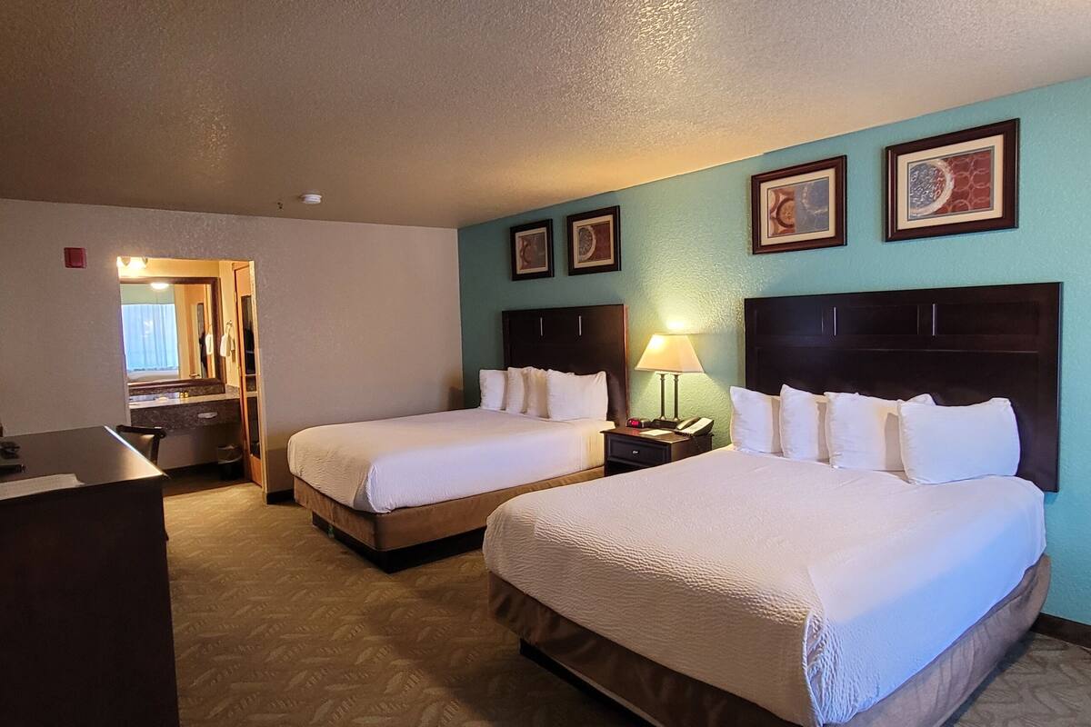 Quarto de hotel com duas camas, uma escrivaninha e um espelho.