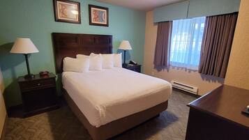Habitación de hotel con una cama grande, dos mesitas de noche con lámparas, un mueble auxiliar, una ventana con cortinas y dos cuadros en la pared.
