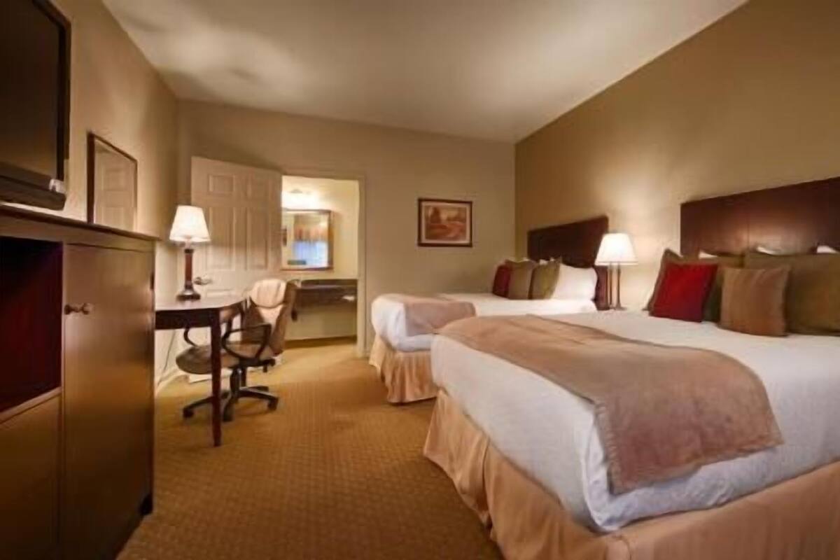 Quarto de hotel com duas camas, uma escrivaninha e uma cadeira.
