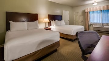 A hotel room with two beds, a desk, a chair, a lamp, and an air conditioning unit.