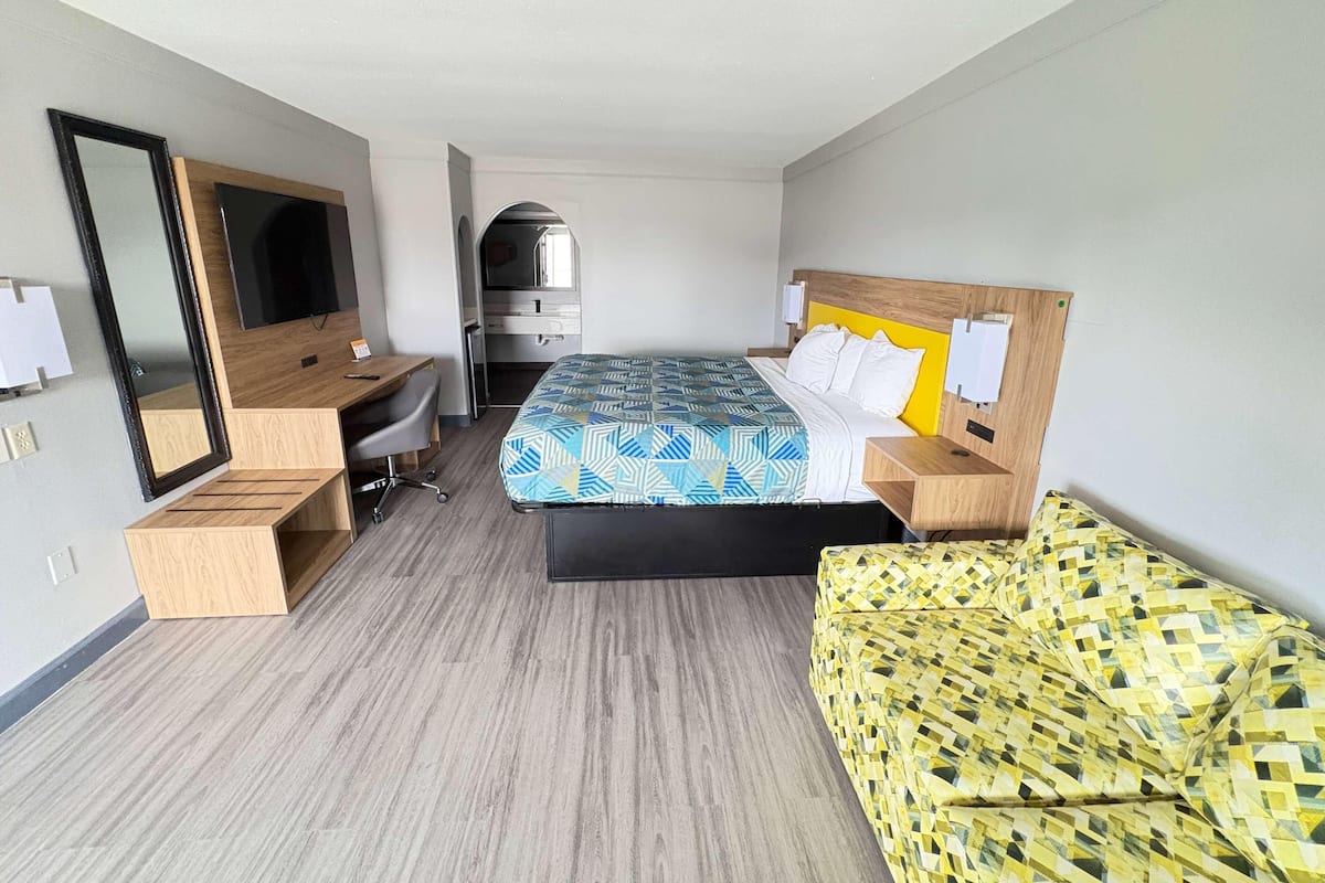 A hotel room with a bed, a desk, a chair, a mirror, and a TV.