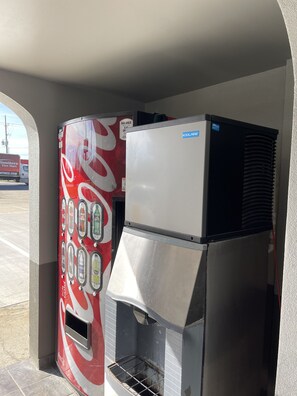 A vending machine with a Coca-Cola logo, a white top, and a metal front panel. - Days Inn by Wyndham Gonzales (Gonzales)